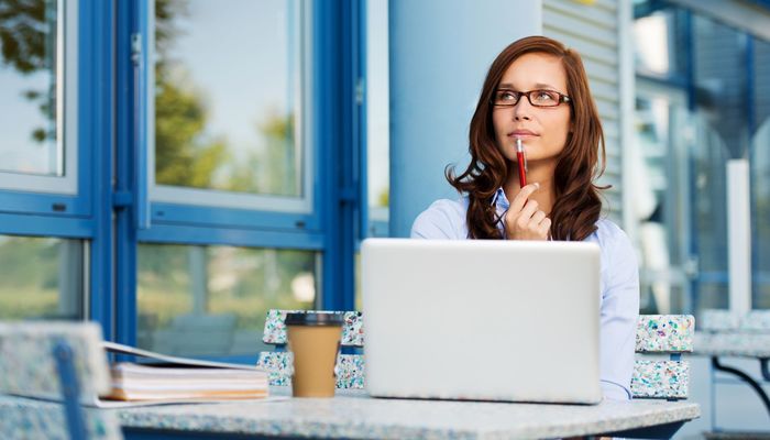 Pretty woman fiddling with pen and thinking over a subject while sitting in some coffee shop with her laptop