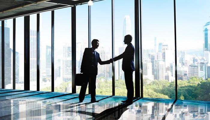 Two business partners shaking hands in a boardroom with a view of the city