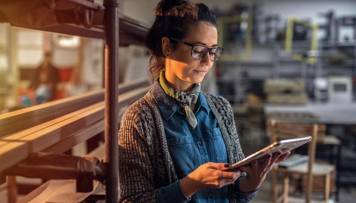 Middle aged beautiful woman standing in her work shop at looking at the tablet.