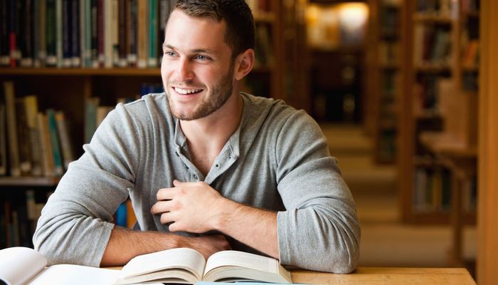 A student sat in a library thinking and smiling
