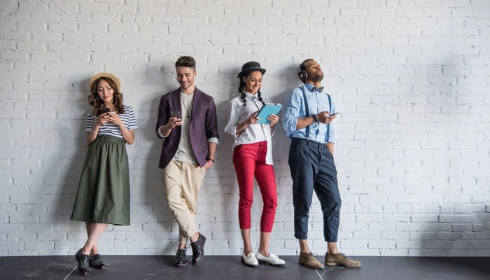 A group of millennials stood against a wall on their phones