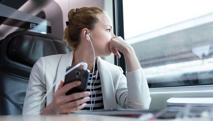 Woman on train listening to a podcast on her headphones while looking out of the window